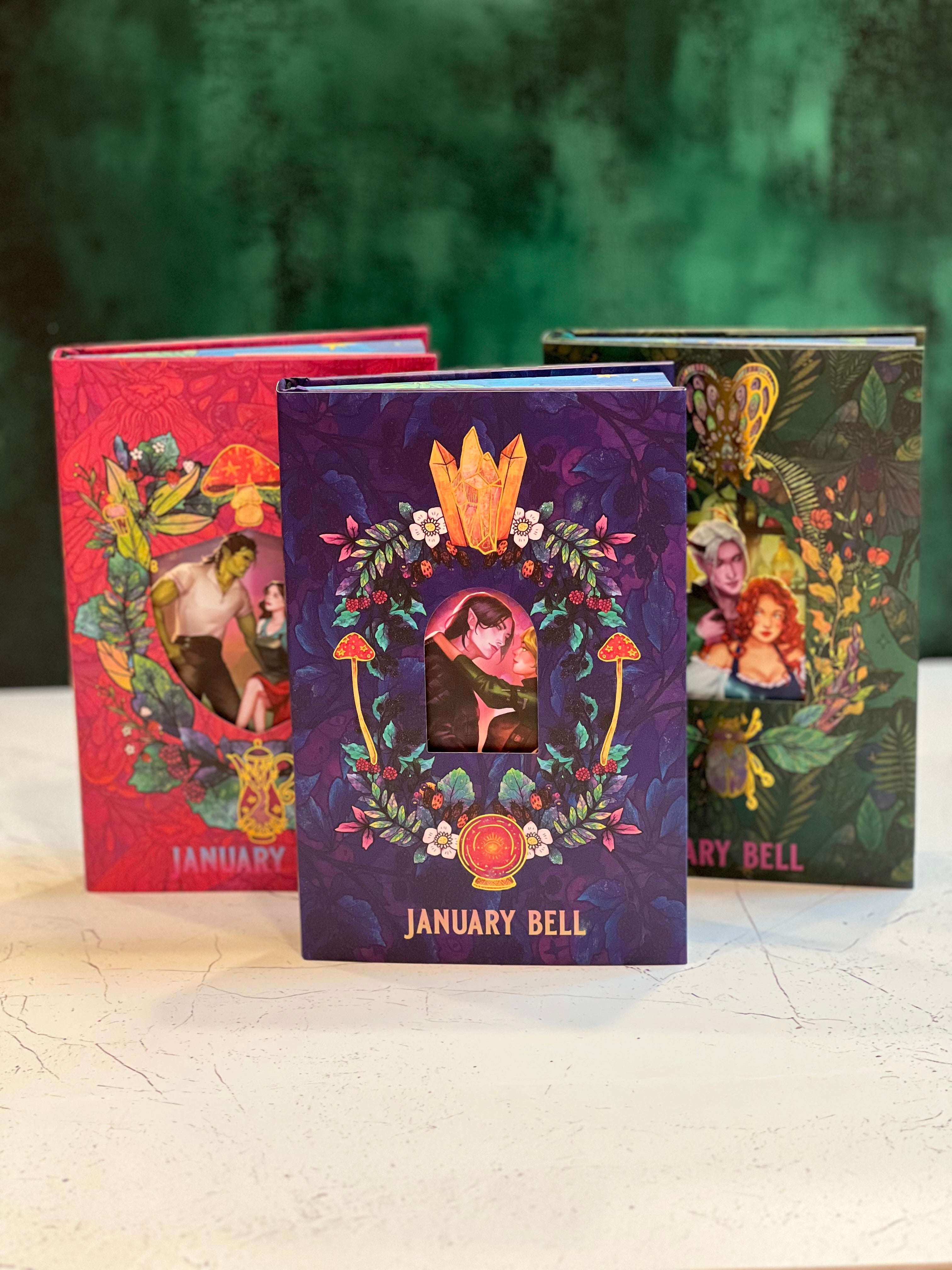 Three colorful books by 'January Bell' with fantasy-themed illustrations on a wooden surface.